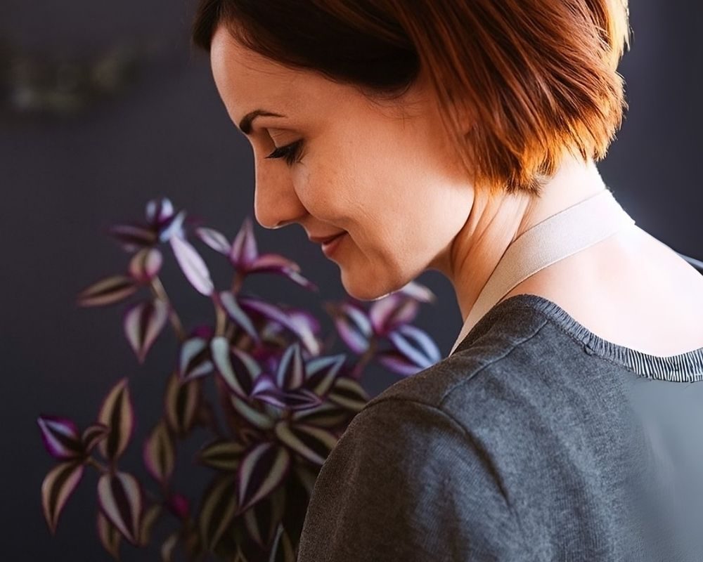 Smiling woman standing near a Wandering Jew plant indoors